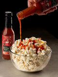 Hot sauce being poured onto popcorn with a bottle of Ooh La La hot sauce in the background.