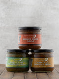 Three jars of Butterfly Bakery of Vermont salsas stacked on a wooden surface with a gray background.