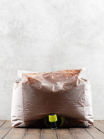 5 liter plastic bag filled with caramel sauce with a nozzle sticking out on a wooden surface against a light gray background