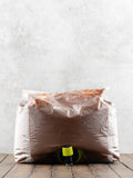 5 liter plastic bag filled with caramel sauce with a nozzle sticking out on a wooden surface against a light gray background